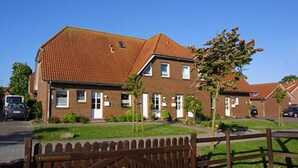 Een tweelaags bakstenen huis met een dak van rode tegels, een voortuin en een kleine tuin.
