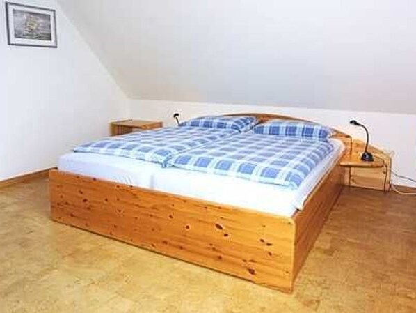 A single bed with a wooden frame and a blue and white checkered bedspread in a room with white walls and a sloped ceiling. - Apartment in the guest area 2 A - Apartment Im Gastfeld 2 A (Werdum)