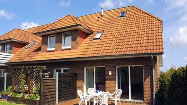 Een tweelaags huis met een pannendak, een terras met tuinmeubilair en een tuin.