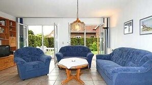 Een woonkamer met een blauwe bank, twee fauteuils, een salontafel en een televisie.