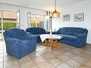Ein Wohnzimmer mit blauem Sofagarnitur, einem Holztisch und einer hängenden Leuchte.