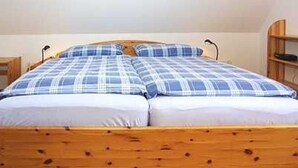 Een eenpersoonsbed met een houten hoofdbord en een blauw-witte geruite sprei.