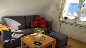 A living room with a grey sofa, a wooden coffee table, and a window with a view of the sea.