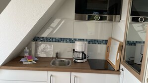 A compact kitchen with white cabinets, a stainless steel sink, a coffee maker, and a microwave.