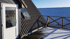 A wooden deck with a snow-covered floor, a glass door with a logo, and a view of the sea.