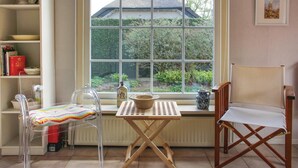 Une pièce dotée d’une grande fenêtre, d’une table en bois, d’une chaise transparente, d’une chaise en bois et d’une bibliothèque contenant des livres et des objets décoratifs.