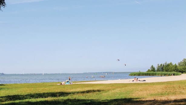 Une plage où l’on voit des gens se prélasser au soleil et nager, avec des éoliennes en arrière-plan.