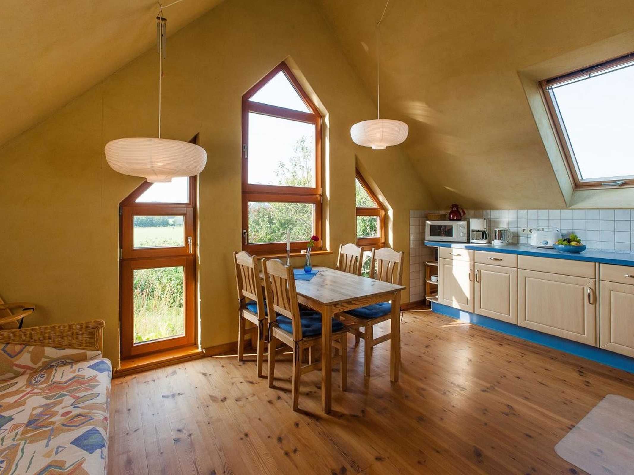 A cozy kitchen with wooden flooring, a dining table with chairs, and a large window providing natural light.