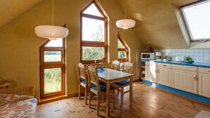 Eine gemütliche Küche mit Holzboden, einem Esstisch mit Stühlen und einem großen Fenster, das viel Tageslicht hereinlässt.