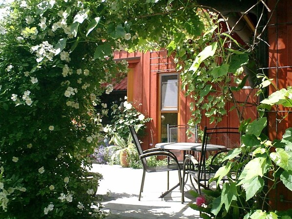 A patio with a table and chairs, surrounded by lush greenery and flowering plants.