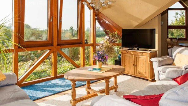 Ein geräumiges Schlafzimmer im Loft-Stil mit großen Fenstern, Holzbalkendecke, einer Kronleuchter, einem Fernseher und einer gemütlichen Sitzecke.