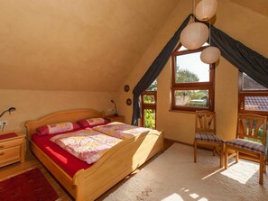 A cozy bedroom with a wooden bed, a desk, and a chair, featuring a large window and a sloped ceiling.