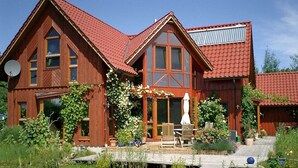 Ein Holzhaus mit rotem Dach, großen Fenstern und einem Steg, der sich ins Wasser erstreckt.