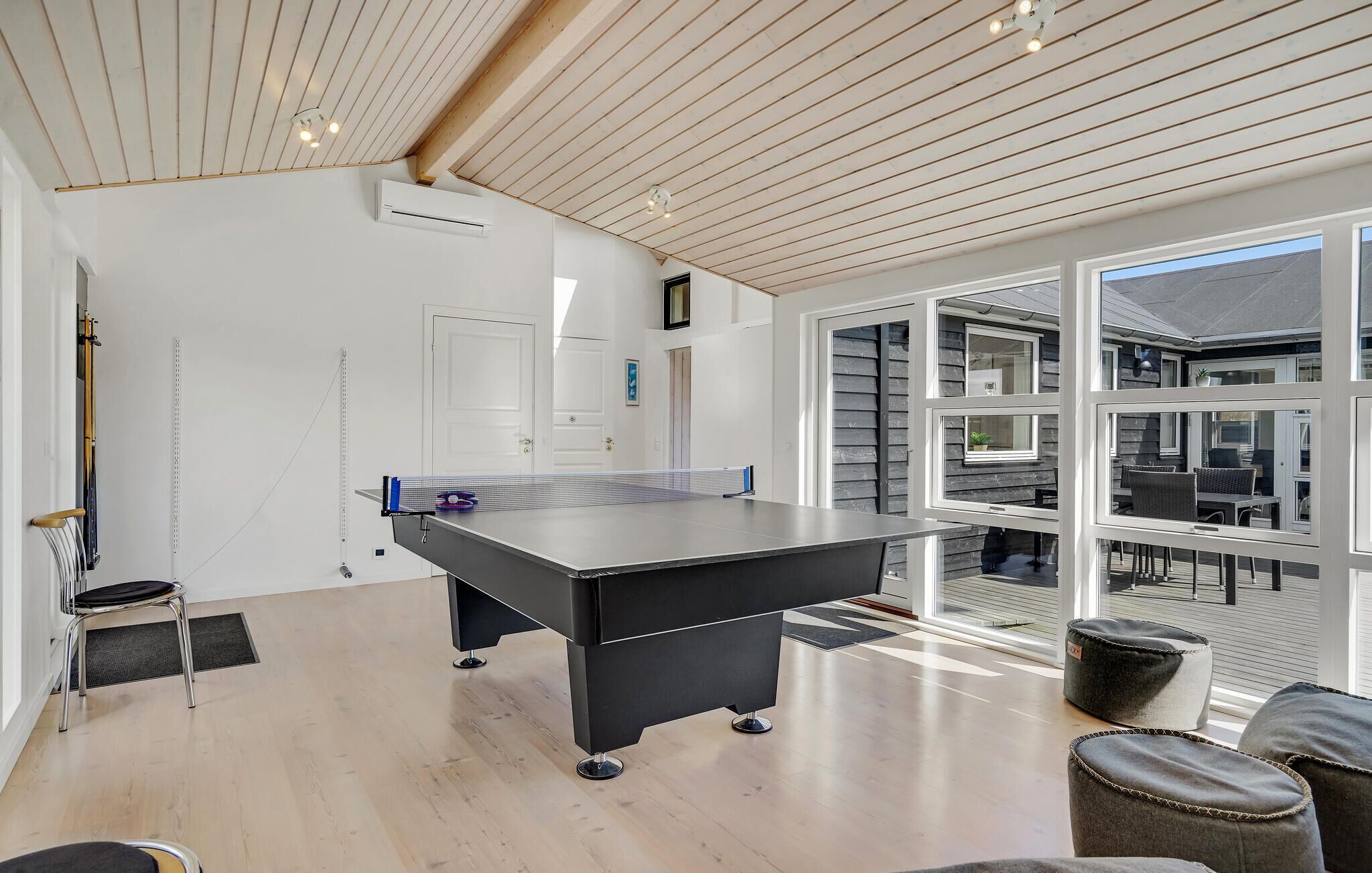 A ping pong table in a room with a wooden ceiling, large windows, and a view of the outside.