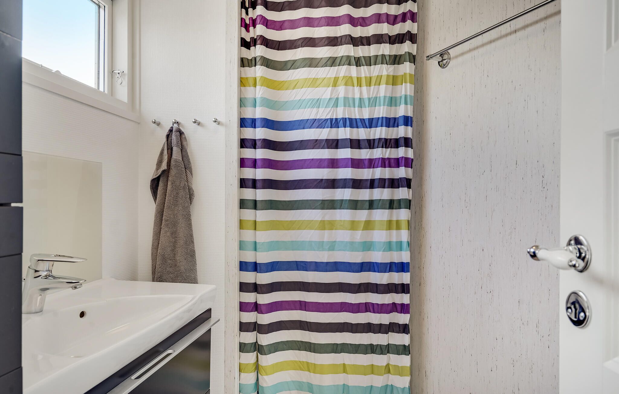 Ein Badezimmer mit einem weißen Waschbecken, einem Handtuch an der Wand und einem gestreiften Duschvorhang.