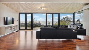 Un salon moderne doté d’un grand téléviseur à écran plat, d’un canapé foncé et d’une grande fenêtre offrant une vue sur la mer.