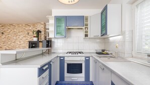 Una cocina compacta con estufa a gas, horno y un lavamanos pequeño. Hay armarios con pomos azules y una encimera con una planta y una tetera.