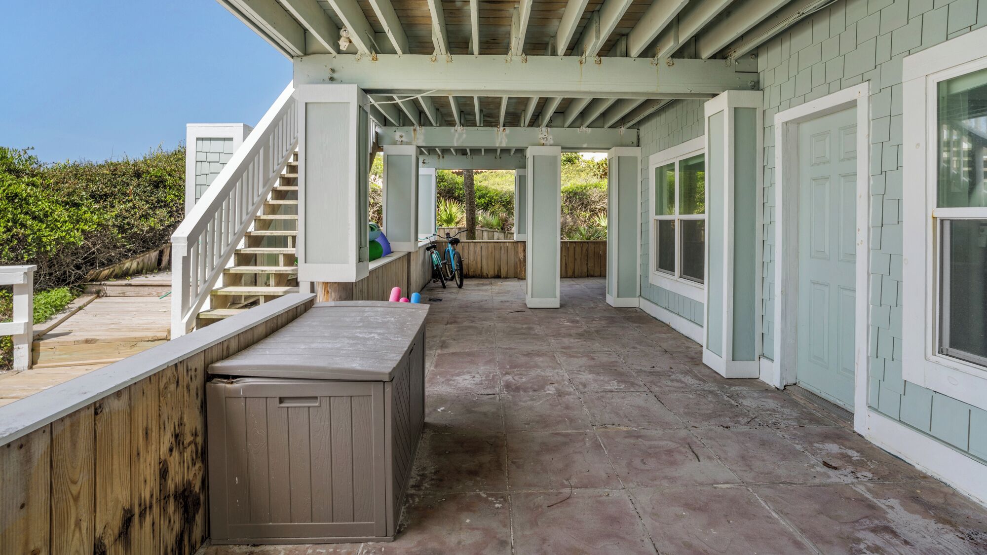 A covered patio area with a wooden deck, a hot tub, and a staircase leading to an upper level.