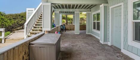 A covered patio area with a wooden deck, a hot tub, and a staircase leading to an upper level.