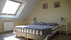 Un dormitorio con techo inclinado, un tragaluz, una cama con ropa de cama a rayas, dos mesitas de noche con lámparas y dos cuadros en la pared.