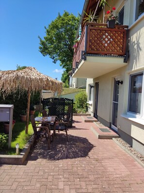 Une terrasse avec une table et des chaises, un parasol en chaume et une clôture en bois.