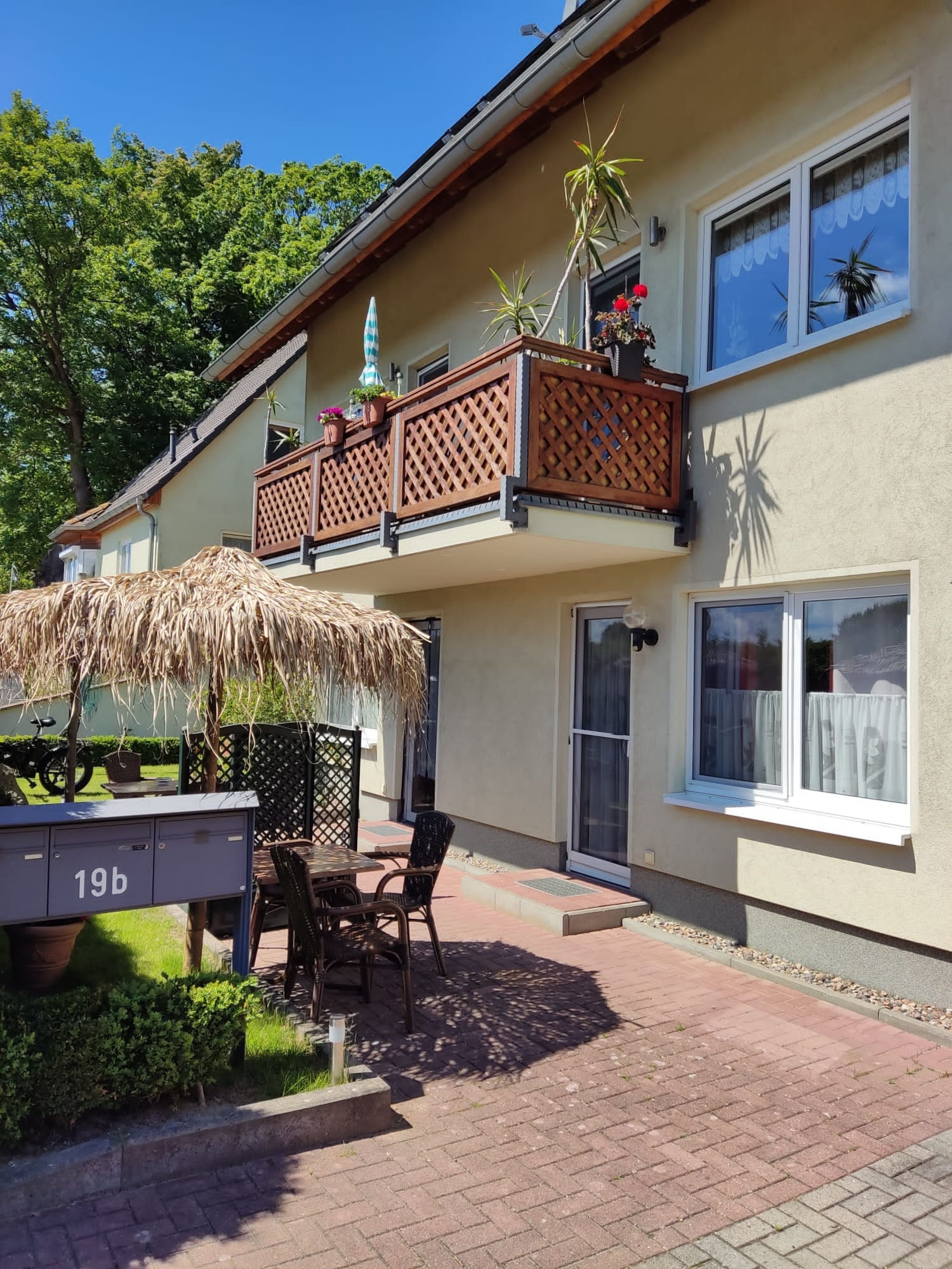 A two-story building with a balcony, a thatched umbrella, and a small outdoor seating area.