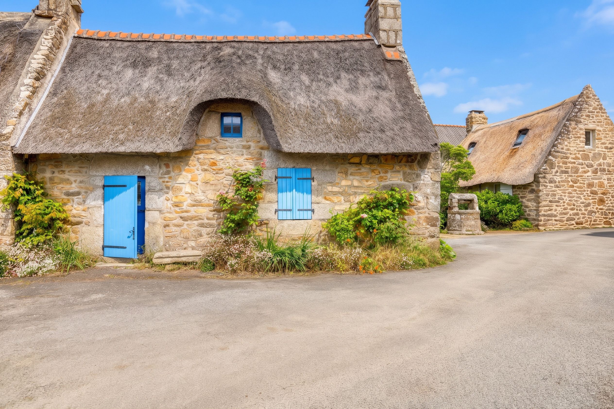 A stone cottage with a thatched roof, blue shutters, and a small window.