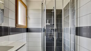 A modern bathroom with a glass shower enclosure, white and black tiled walls, and a wooden-framed mirror. - Homerez - House - Nevez, Enclosed (Nevez)