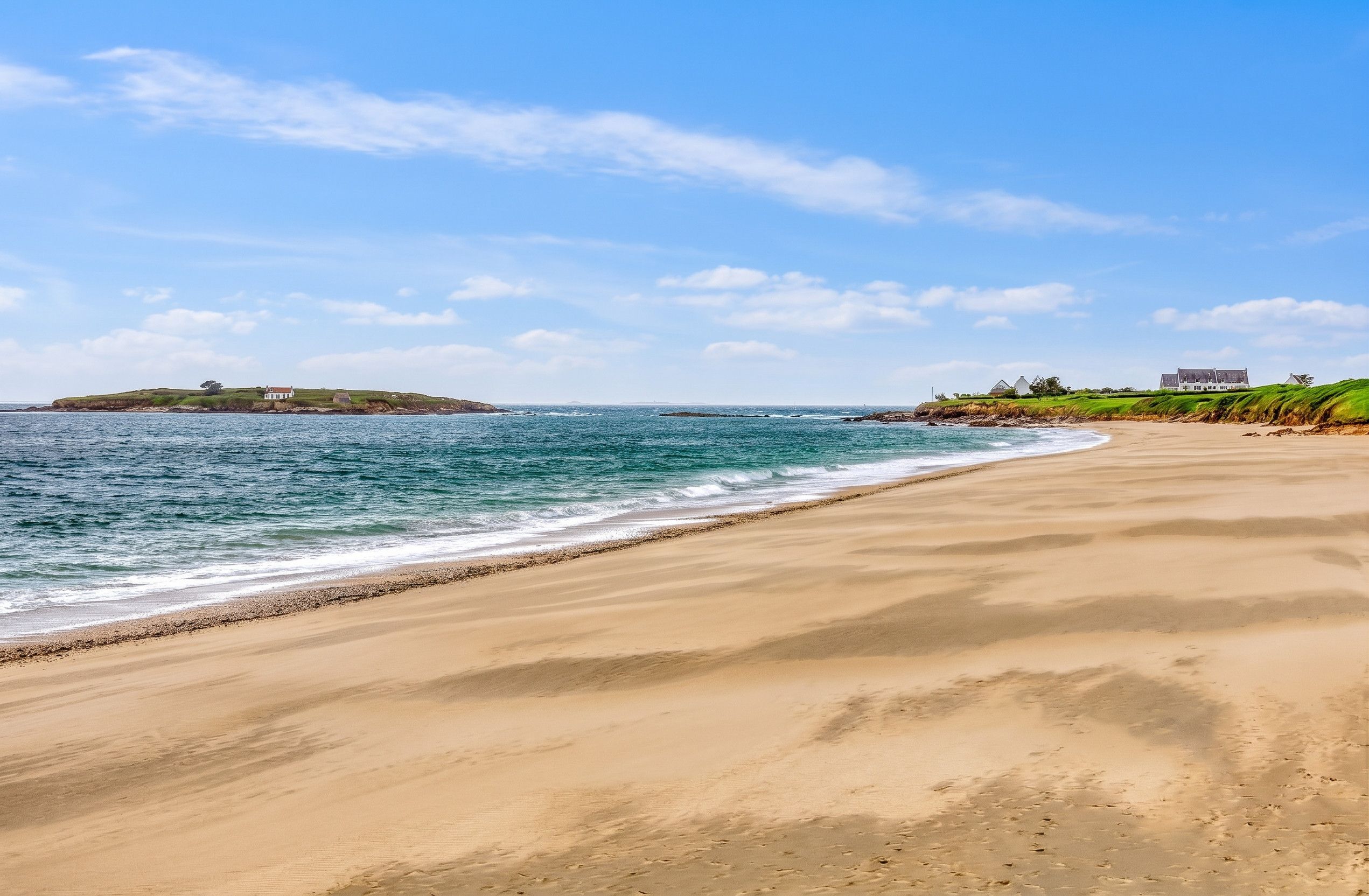 A beach with a sandy shore and a grassy hill with buildings in the distance.