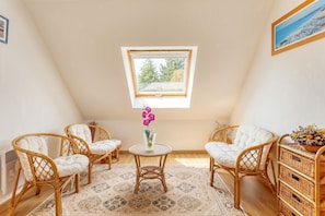 A cozy room with a sloped ceiling, a small table with chairs, and a window with a view of trees.