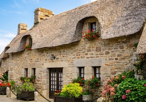 A stone building with thatched roofs, multiple windows, and flower boxes.