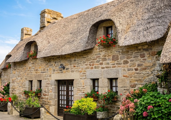 A stone building with thatched roofs, multiple windows, and flower boxes.