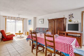 A dining area with a red and white checkered tablecloth, wooden chairs, a television, and a cabinet with decorative items.
