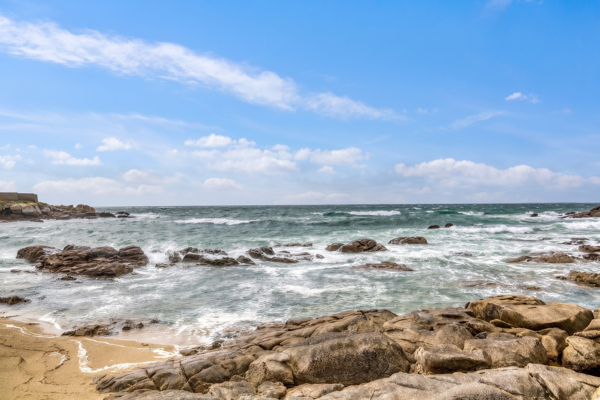 A rocky beach with waves crashing against the shore under a clear sky.