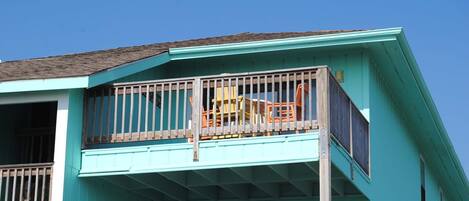 A turquoise two-story building with a balcony featuring a wooden railing and a yellow chair.