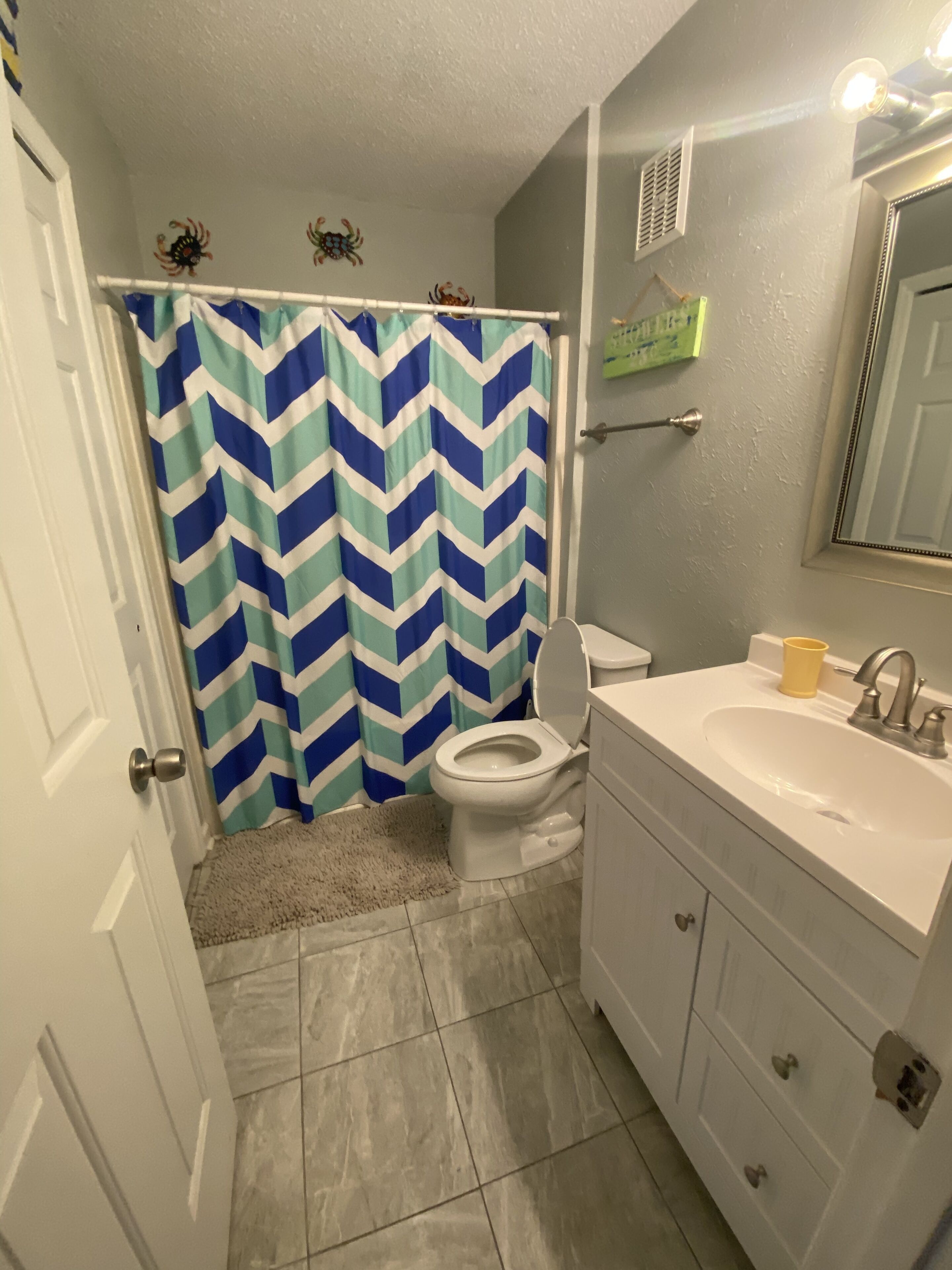 Un baño con inodoro blanco, lavamanos con espejo y cortina de ducha con estampado de chevrón.