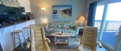 A living room with two beige armchairs, a sofa, a coffee table, and a painting on the wall.