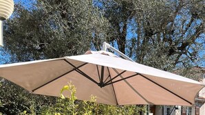 Un patio al aire libre con una mesa, sillas, una sombrilla grande y una planta en maceta.