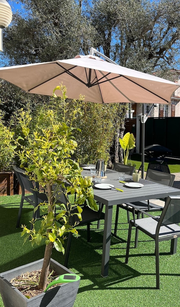 An outdoor patio with a table and chairs, a large umbrella, and a potted plant.