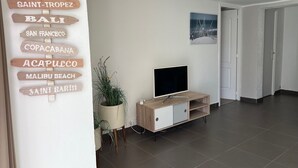 Una sala de estar moderna con un televisor sobre un mueble de madera, una planta en maceta y una pared con letreros de madera que indican varios destinos.