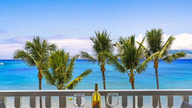 A balcony with a view of the ocean, palm trees, and a bottle of wine. - Stunning Views & Tropical Tranquility 429 LS (Lahaina)