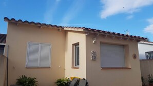 A two-story building with a tiled roof, a small window with shutters, and a door.