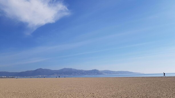 A wide sandy beach with a clear sky and distant mountains.