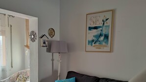 A living room with a grey sofa, a white chair, and a blue and orange striped pillow. There is a framed picture of a whale on the wall.