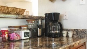 Uma bancada de cozinha com equipamento para fazer café, açúcar e grãos de café.