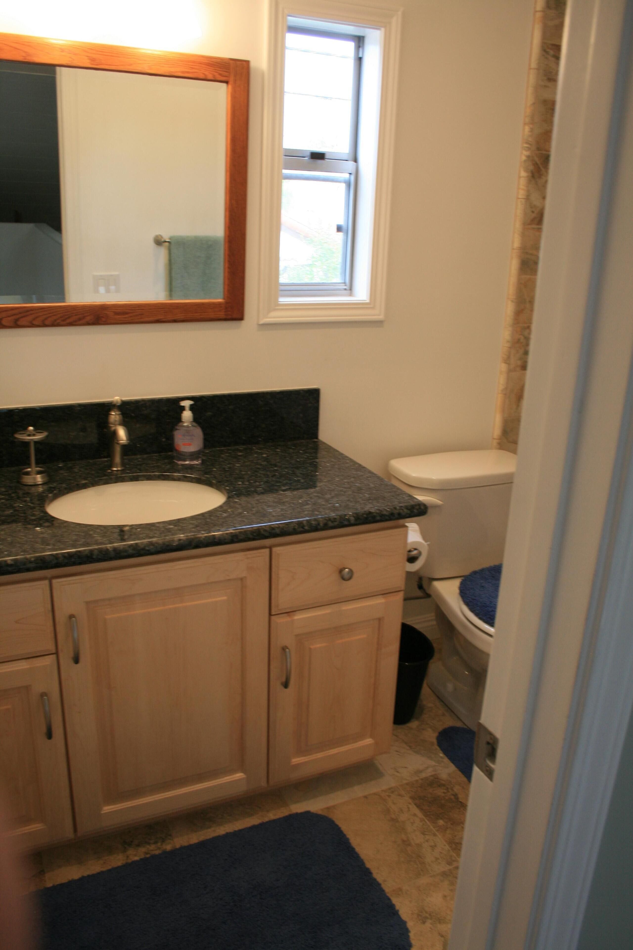 A bathroom with a sink, mirror, toilet, and a window.