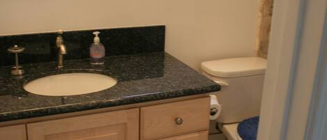 A bathroom with a sink, mirror, toilet, and a window.