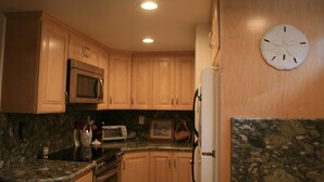 A kitchen with wooden cabinets, a microwave, a toaster, and a refrigerator. - Steps from watching Sunsets in the Sand (Carpinteria)