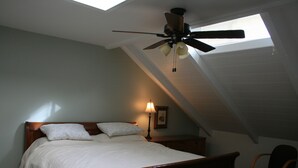 A bedroom with a sloped ceiling, a bed with white linens, a nightstand with a lamp, and a ceiling fan. - Steps from watching Sunsets in the Sand (Carpinteria)