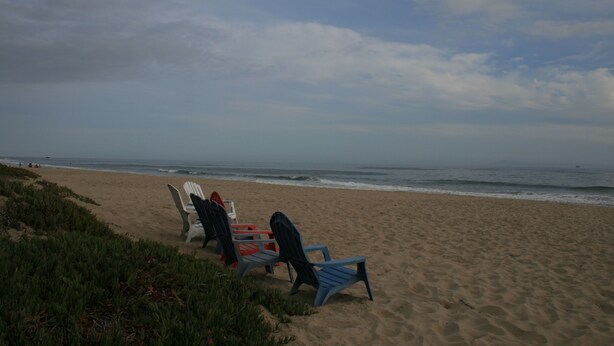 A beach with several Adirondack chairs lined up facing the ocean. - Steps from watching Sunsets in the Sand (Carpinteria)